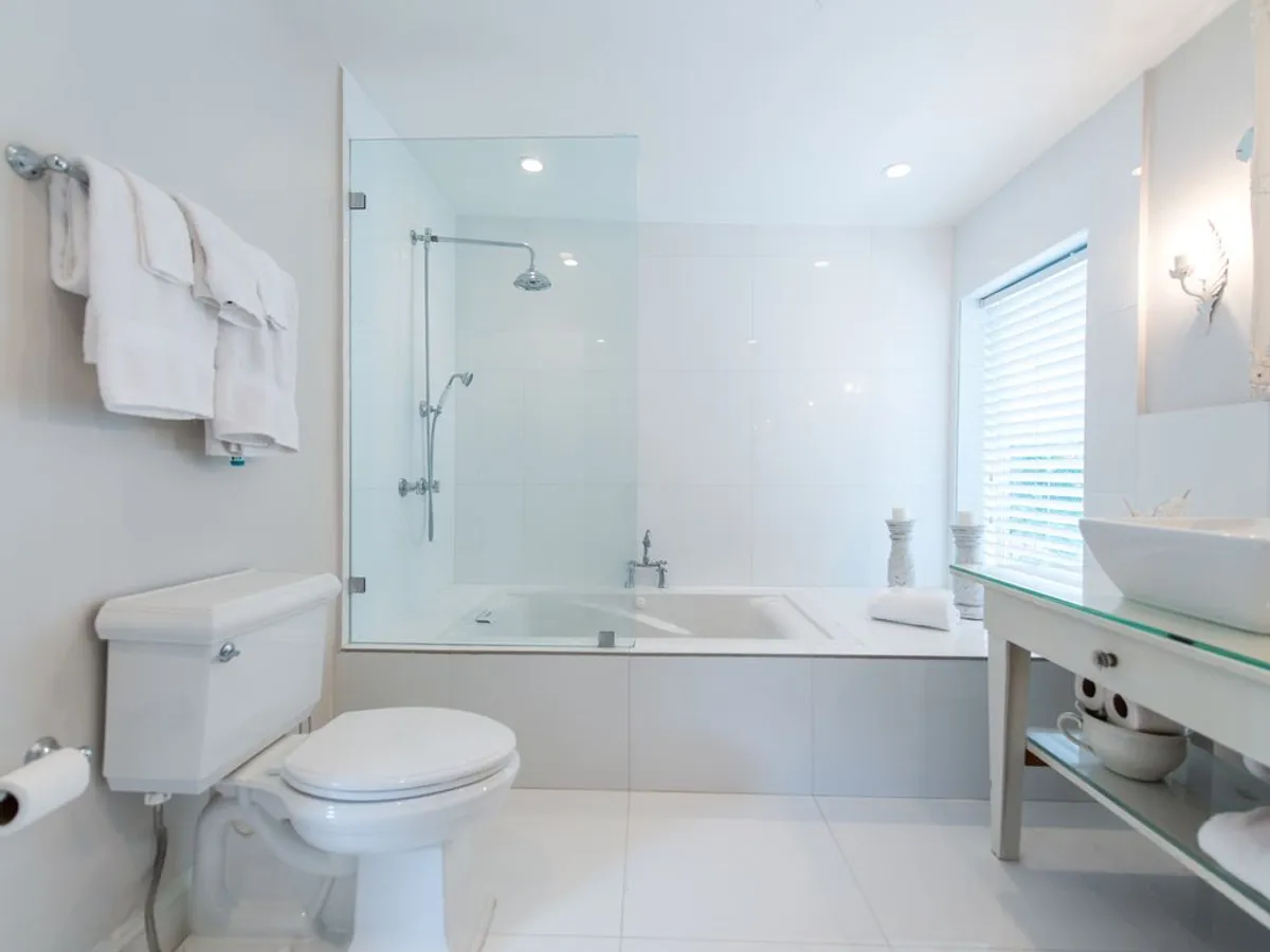 A modern bathroom with a bathtub and shower combination, towels on a rack, a toilet, and a sleek glass countertop sink. The space is designed for relaxation and personal care, with a refreshing and serene ambiance.
